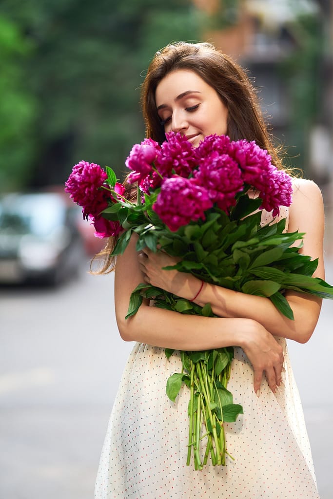 Beautiful Young Brunette Woman In A Nice Spring Dress With A Bouquet Of Pions.